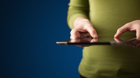 Close up of hand holding digital touchpad tablet device on background