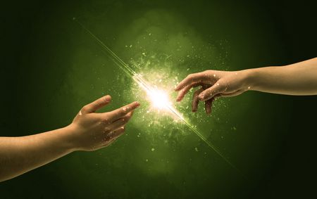 Two naked male hands about to touch, lighting the spark with modest explosion in front of green background concept
