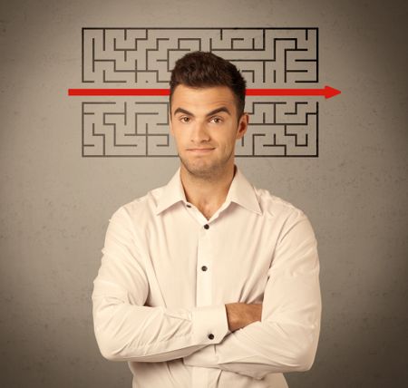 A young handsome business person making facial expression and solving maze with red arrow in front of clear, empty concrete wall background concept