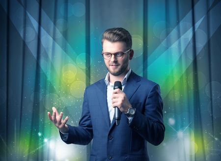 Businessman speaking into microphone with blue curtain behind him