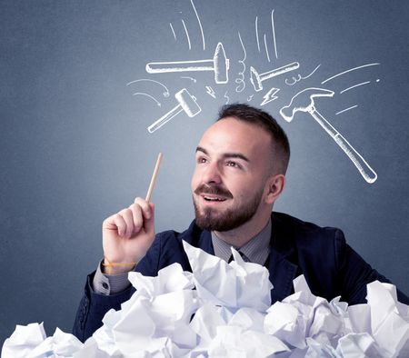 Young businessman sitting behind crumpled paper with drawn hammers hitting his head