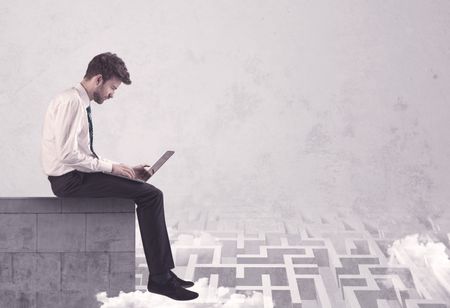 Business worker sitting on concrete building edge, thinking of solving a maze concept with labyrinth and clouds