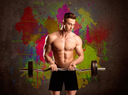 A muscular young bodybuilder lifting weight and showing his hot body with muscles in front of an urban painted wall concept
