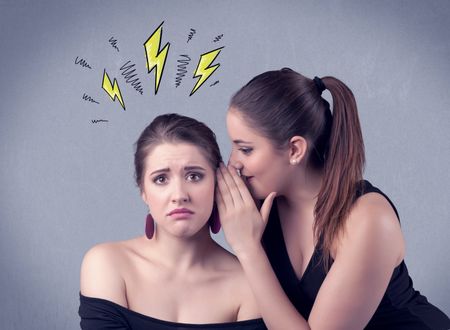 A beautiful girl in black dress sharing secrets to her girlfriend concept with drawn energetic electric yellow signs above her head on the wall background.