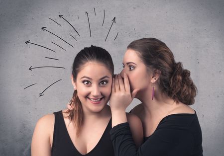 A cute teen caucasian girl telling secret things to her girlfriend dressed in black dress concept with drawn lines, curves, spirals on grey wall background.