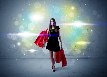 A beautiful young girl standing with long hair and red shopping bags in front of colorful light bokeh urban wall background concept