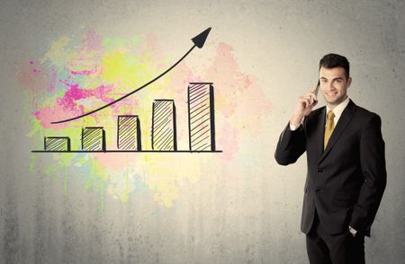 An elegant businessman standing in front of a grey wall with colorful growing chart drawing concept