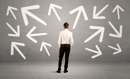 An elegant businessman standing with his back in front of urban wall full of arrows pointing in different directions concept