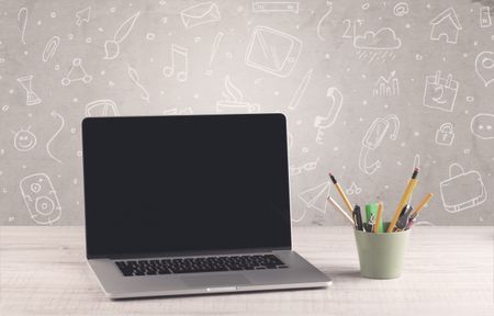 Close up of business office desk with laptop tablet in front of brown wall background full of drawn communication icons and school items concept