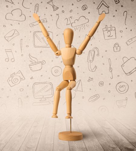 Wooden mannequin posed in front of a greyish background with mixed media scribbles behind it