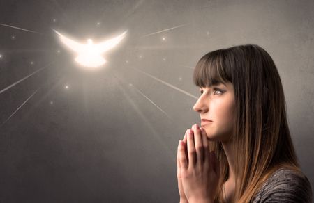 Young woman praying on a grey background with a sparkling bird above her