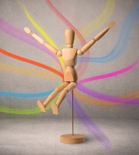 Wooden mannequin posed in front of a greyish background with colorful lines behind it