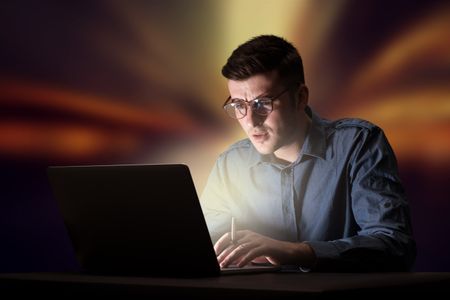 Young handsome businessman working late at night in the office with warm lights in the background