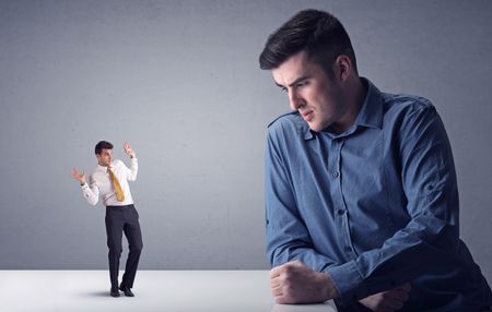 Young professional businessman being angry with an other miniature businessman in front of a grey background