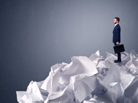 Thoughtful young businessman standing on a pile of crumpled paper with a light grey background