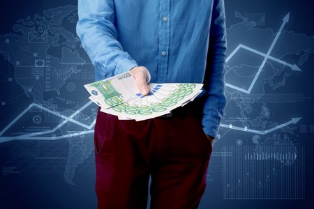 Young businessman holding large amount of bills with blue charts in the background