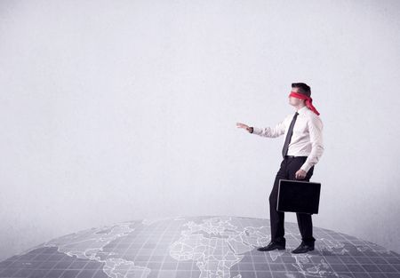 Young blindfolded businessman steps on a grey world map