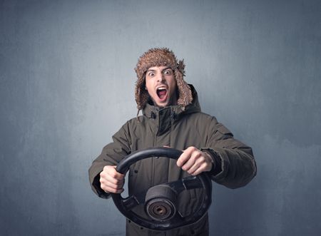 Young man holding black steering wheel on a blueish gray background