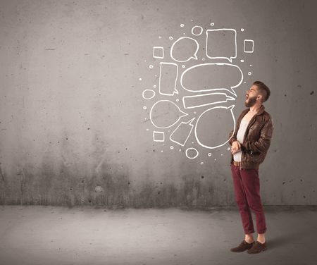 A comic hipster guy shouting in front of grey urban concrete wall with drawn empty text bubbles around his mouth concept
