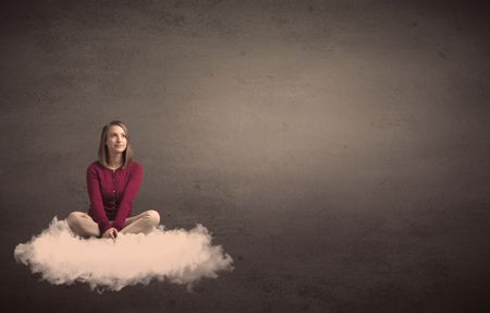 Caucasian woman sitting on a white fluffy cloud daydreaming beside a plain grunge background