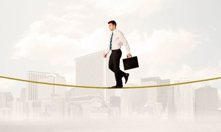 A young elegant businessman walking on tight golden rope in front of city buildings landscape background concept