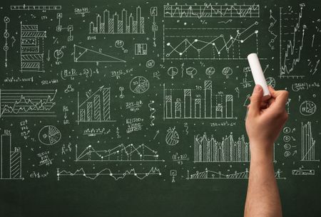 A hand drawing lines, pie charts, graphs on a green blackboard with a chalk