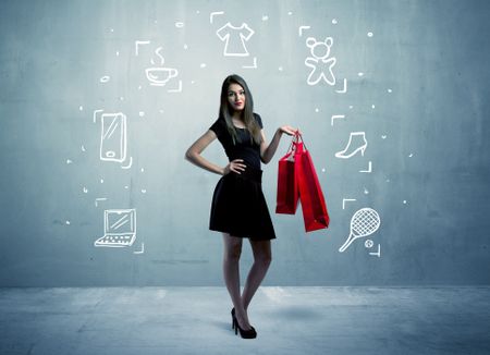 A beautiful young girl in black standing with red shopping bags in front of urban wall background and laptop, shoes, tennis icons concept