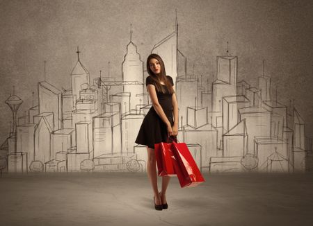 An attractive young lady standing with red shopping bags in front of drawn city landscape silhouette concept