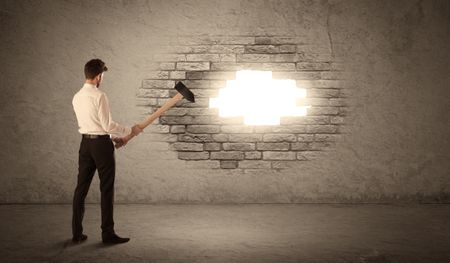 Business man hitting brick grungy wall with hammer and opening a hole