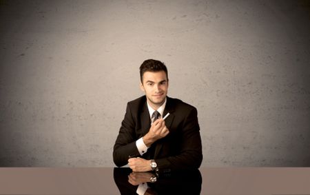 A happy businessman sitting at desk in front of clear grey empty background and drawing around himself with a white chalk concept