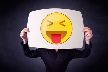 Young businessman hiding behind a playful emoticon on cardboard