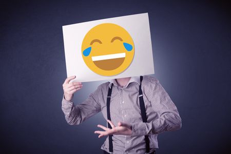 Young businessman hiding behind a laughing emoticon on cardboard