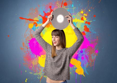 Young lady holding vinyl record on a grey background with colorful splashes behind her 