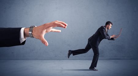 Young miniature businessman running from a big hand with blueish background