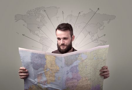 Handsome young man holding a map with world map and arrows behind him