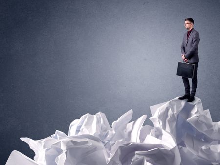 Thoughtful young businessman standing on a pile of crumpled paper 