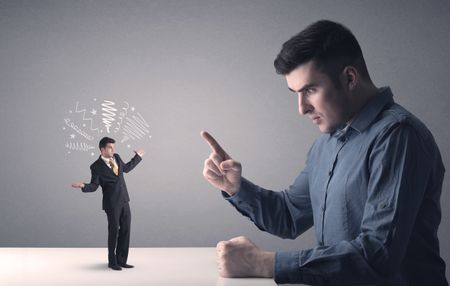 Young professional businessman being angry with an other miniature businessman who has scribbles above his head