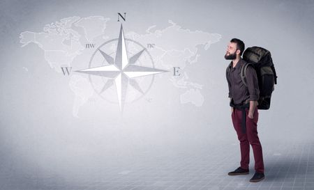 Handsome young man standing with a backpack on his back and a compass and a world map in the background