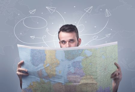 Handsome young man holding a map with drawn paper planes flying behind him