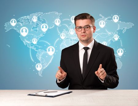 Young handsome businessman sitting at a desk with a blue world map behind him