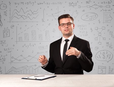 Young handsome businessman sitting at a desk with white charts behind him