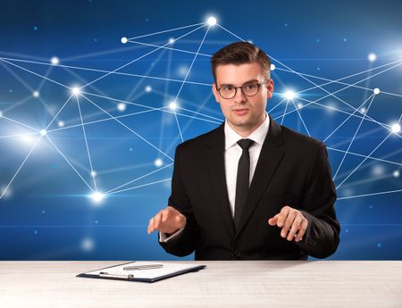 Young handsome businessman sitting at a desk with a blue connection graphic behnid him 