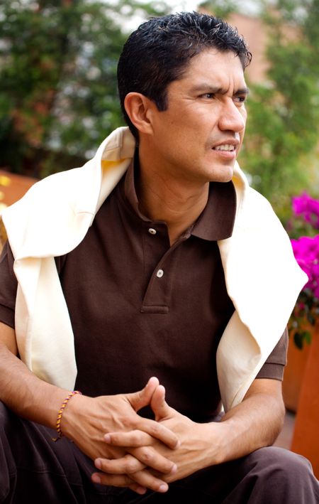 casual man portrait sitting down and looking pensive outdoors