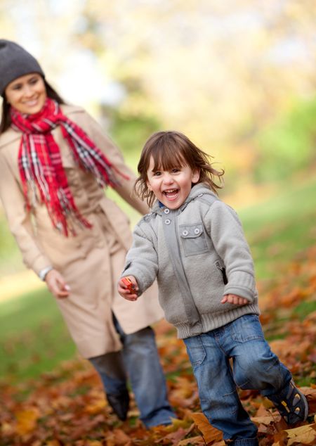Mother and her son running at the park in autumn - family concepts