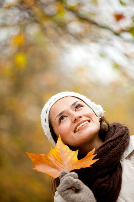 Pensive autumn woman holding a leaf and smiling