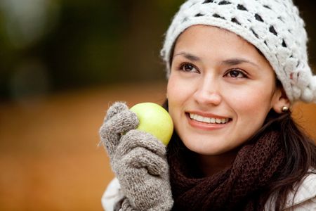 Pensive autumn woman holding an apple and smiling