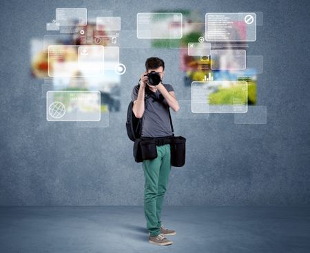 A young professional male photographer holding cameras and taking pictures in front of a blue wall with pictures, icons, text information concept