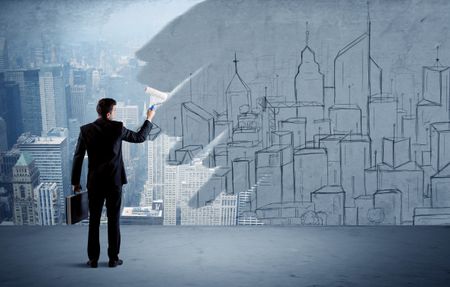A businessman in elegant suit holding a paint roller in his hand and painting drawn city landscape over urban skyscrapers concept