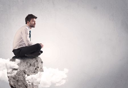 An elegant  smart businessman with laptop sitting in empty grey space on top of a cliff, between clouds concept