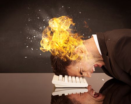 A depressed businessman banging his head in a keyboard and shouting with his head on fire, reflecting on desk